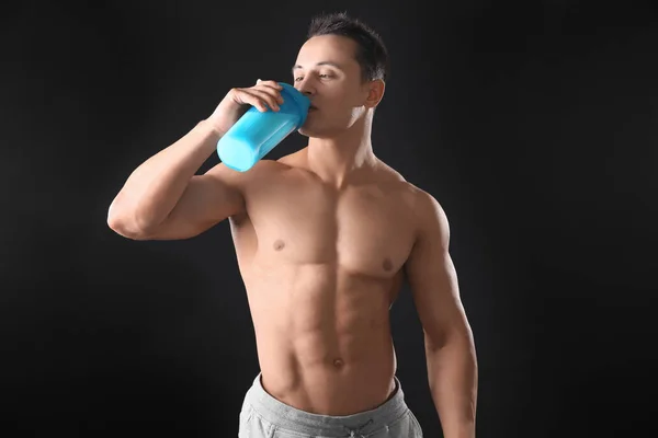 Sportlicher junger Mann trinkt Proteinshake auf schwarzem Hintergrund — Stockfoto