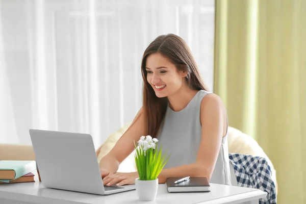 Mulher bonita com laptop moderno sentado à mesa no quarto — Fotografia de Stock