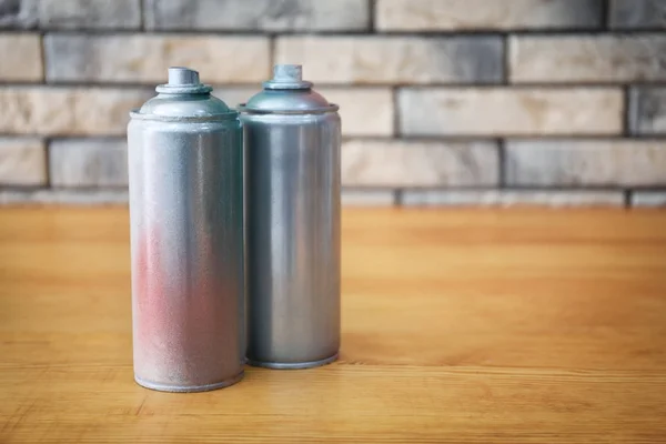 Latas de aerossol de alumínio com tintas em mesa de madeira contra parede de tijolo — Fotografia de Stock