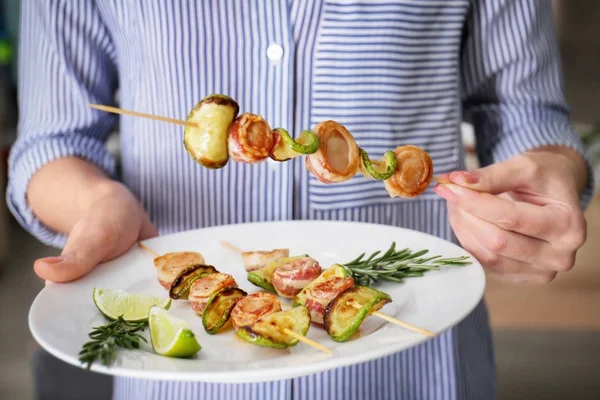 Woman holding bamboo skewer and plate with bacon wrapped scallops — Stock Photo, Image
