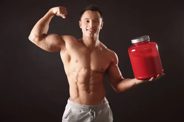 Sportlicher junger Mann mit einem Glas Proteinpuder auf schwarzem Hintergrund — Stockfoto