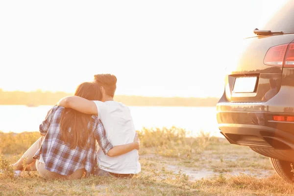 Car yakınındaki çimenlerin üzerinde oturan güzel genç Çift — Stok fotoğraf