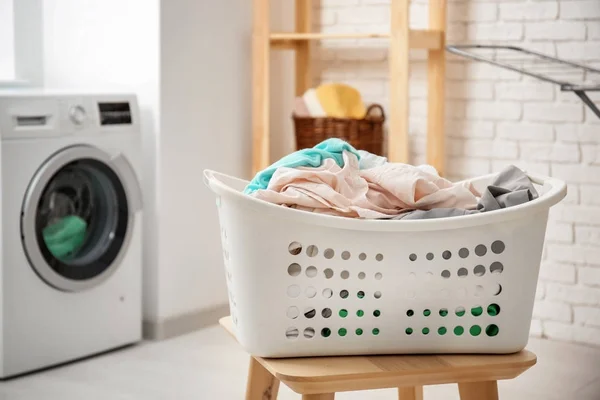 Cesto con lavanderia su sgabello e lavatrice in bagno — Foto Stock