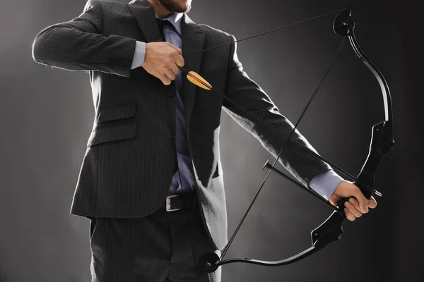 Geschäftsmann übt Bogenschießen auf dunklem Hintergrund — Stockfoto