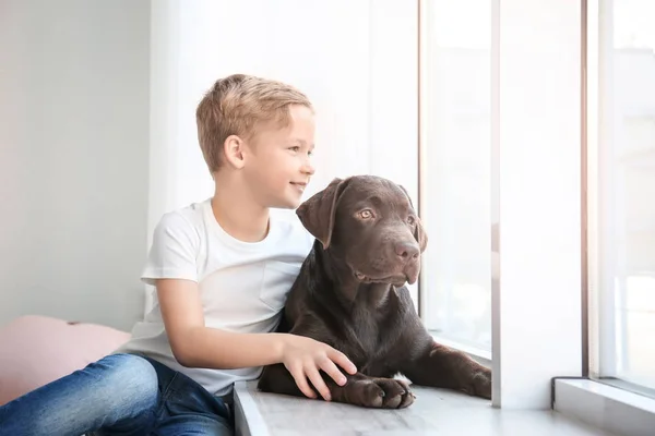 Милый маленький мальчик с собакой у окна дома — стоковое фото