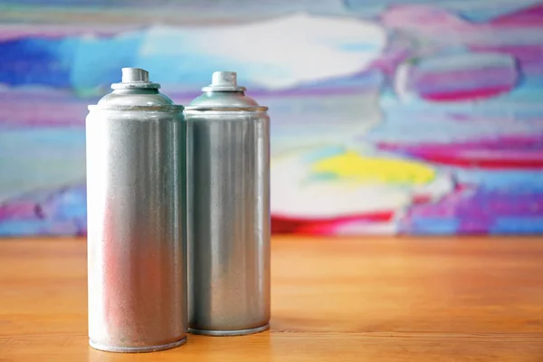 Latas de aerossol de alumínio com tintas na mesa de madeira contra fundo desfocado — Fotografia de Stock