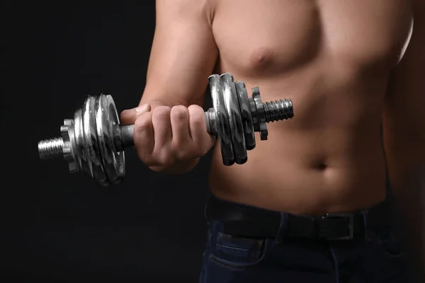 Muscular young bodybuilder with dumb-bell on dark background — Stock Photo, Image