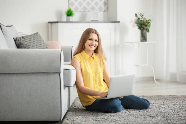 Schöne Frau mit Laptop, während sie sich auf dem Boden in der Nähe von Sofa zu Hause ausruht — Stockfoto