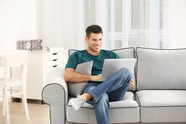 Hombre guapo usando el ordenador portátil mientras descansa en el sofá en casa — Foto de Stock