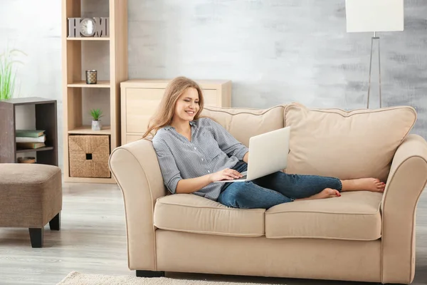 Mulher bonita usando laptop enquanto descansa no sofá em casa — Fotografia de Stock