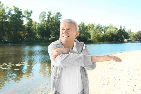 Зрелый человек делает упражнения возле реки — стоковое фото