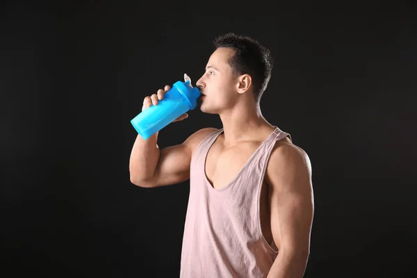 Sportlicher junger Mann trinkt Proteinshake auf schwarzem Hintergrund — Stockfoto