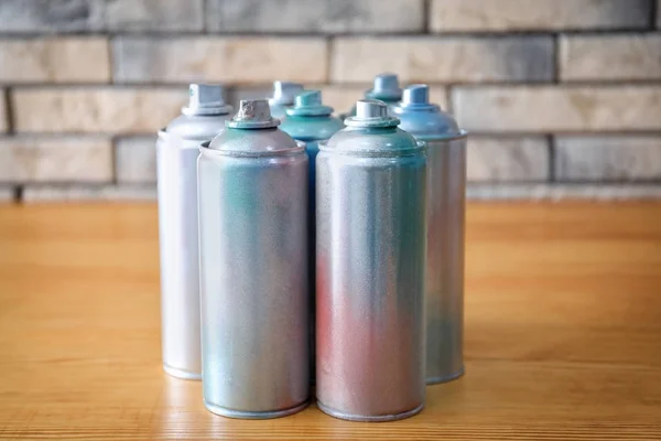 Latas de aerossol de alumínio com tintas em mesa de madeira contra parede de tijolo — Fotografia de Stock