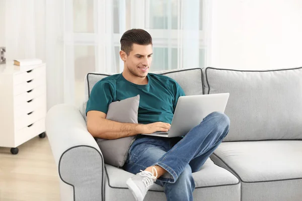 Hombre guapo usando el ordenador portátil mientras descansa en el sofá en casa — Foto de Stock