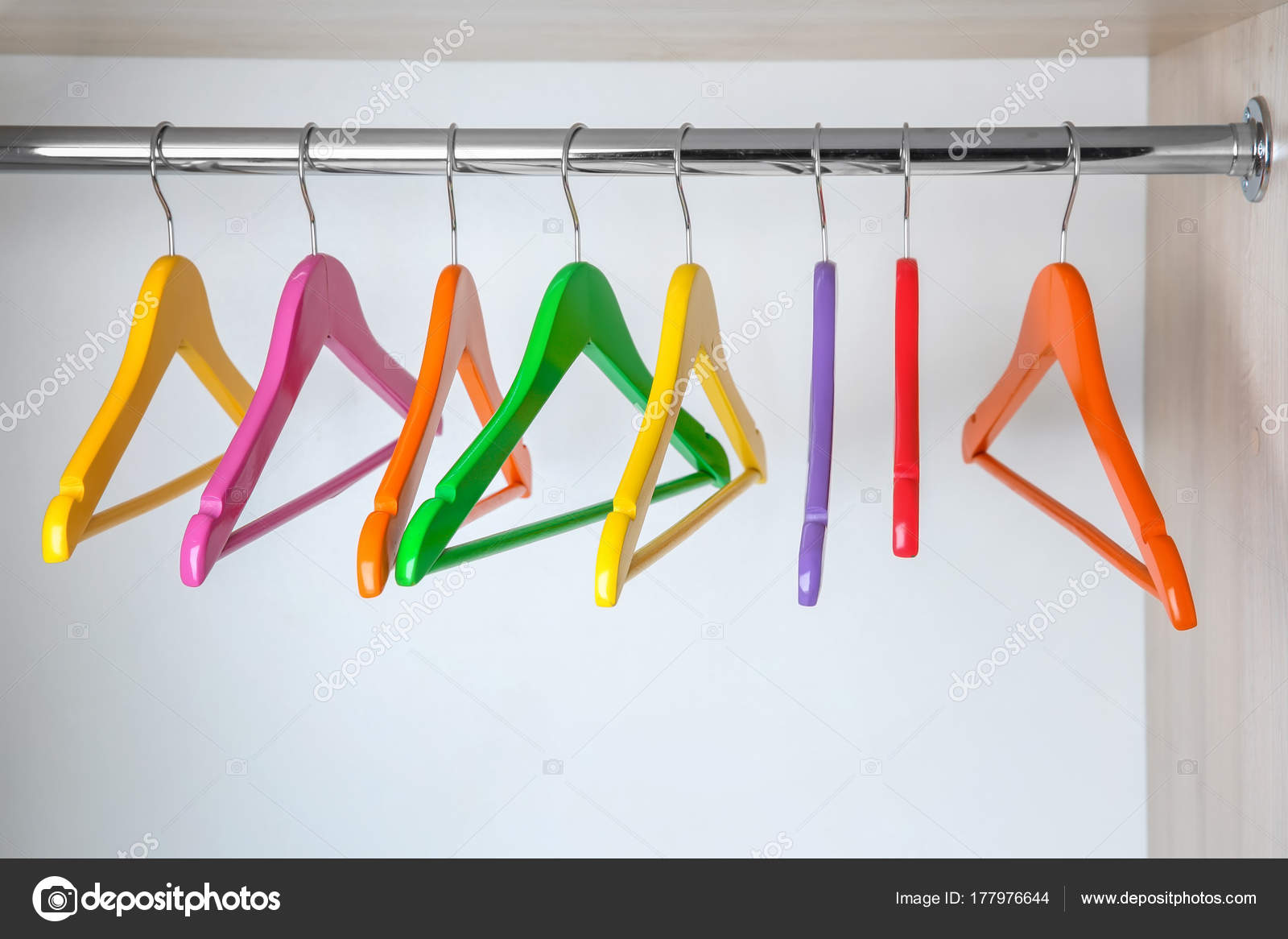 Colorful clothes hangers in empty wardrobe Stock Photo by