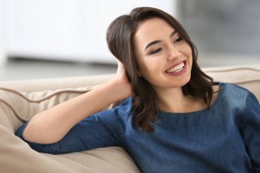 Genç güzel gülümseyen kadın evde koltukta dinleniyor