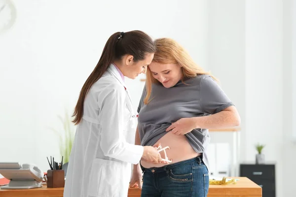 Ung kvindelig læge måler fedt lag af overvægtige kvinde med kaliber i klinikken - Stock-foto