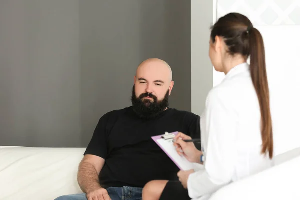 Молодая женщина-врач консультирует толстого мужчину в клинике — стоковое фото