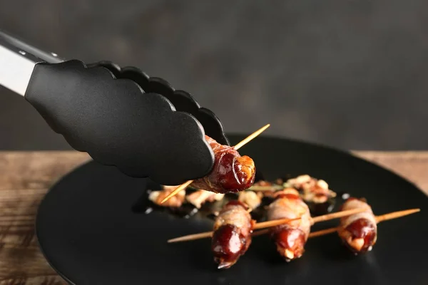 Holding tasty bacon wrapped date with tongs on blurred background, closeup — Stock Photo, Image