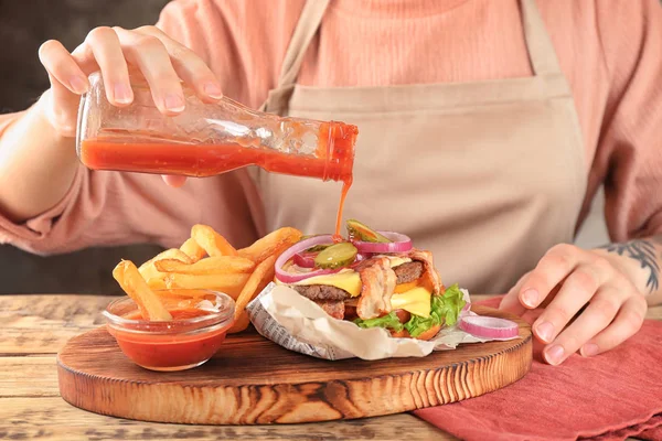 Mujer vertiendo salsa de tomate en hamburguesa doble — Foto de Stock
