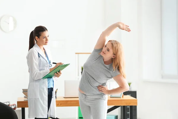 Jovem médica observando mulher com sobrepeso durante o exercício na clínica — Fotografia de Stock