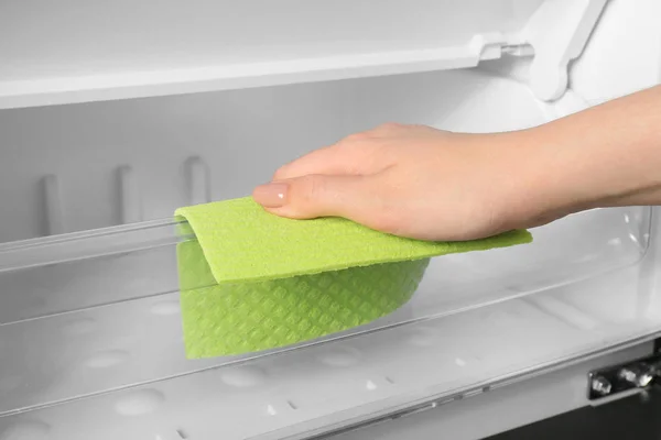 Woman cleaning refrigerator with rag, closeup