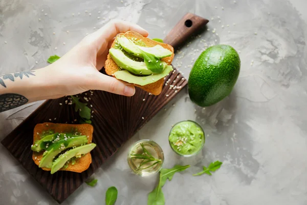 Mujer sosteniendo delicioso pan tostado de aguacate sobre la mesa, vista superior — Foto de Stock