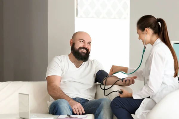 Ung kvinnlig läkare mäta blodtryck för överviktig man i kliniken — Stockfoto