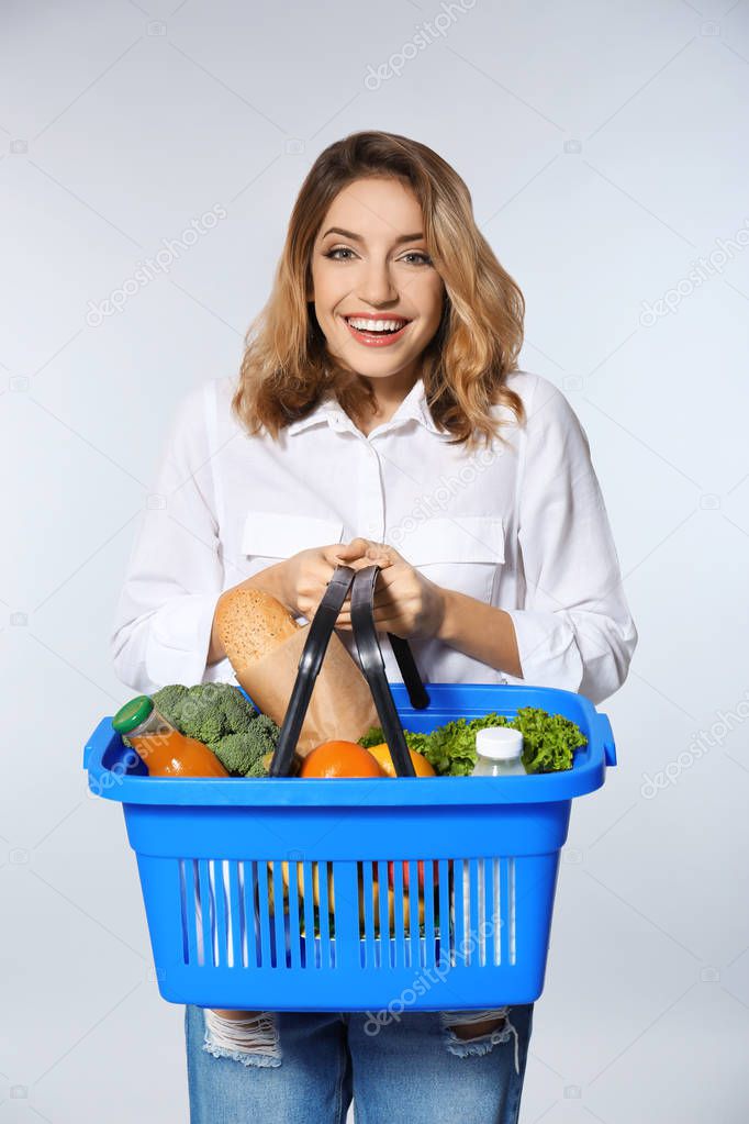 Young woman holding shopping basket with groceries on white background