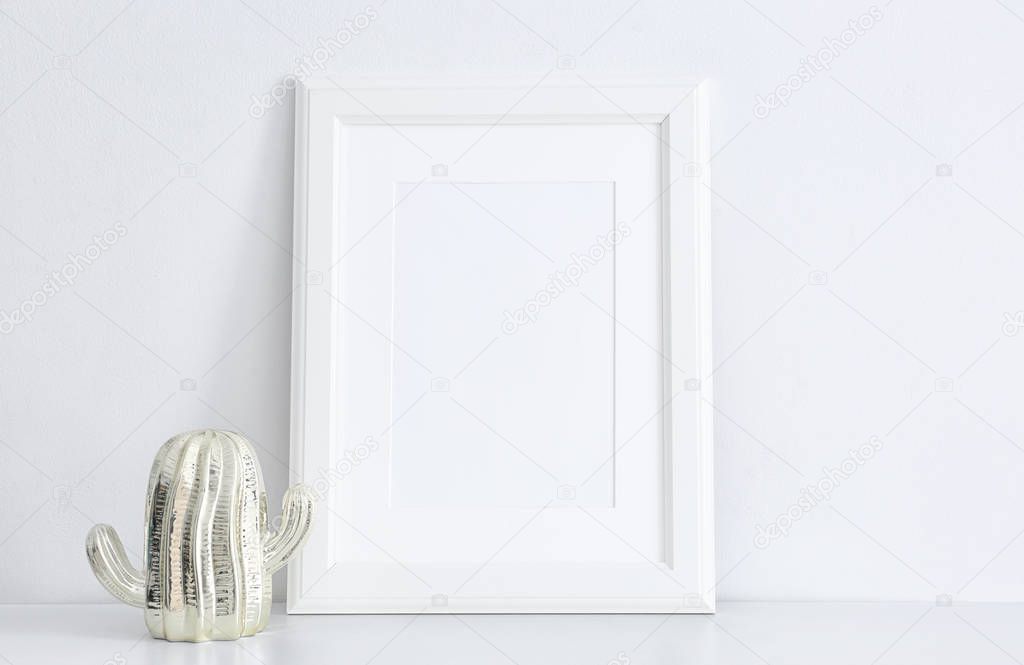 Empty frame and decorative cactus statuette on table near white wall