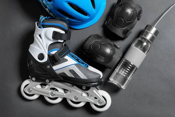 Roller skate, knee pads and bottle of water on grey background