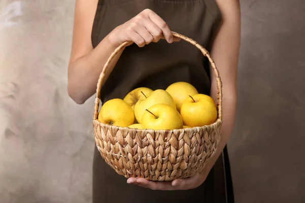 妇女藏品柳条篮子与成熟黄色苹果在颜色背景 — 图库照片