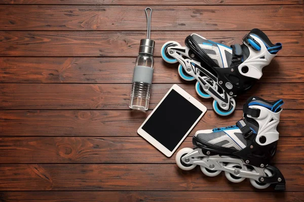 Roller skates, tablet computer and bottle of water on wooden background — Stock Photo, Image