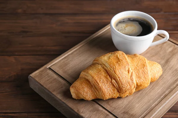 Placa com croissant fresco gostoso e xícara de café na mesa de madeira — Fotografia de Stock