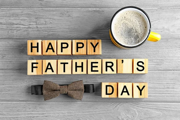 Wooden cubes, bow tie and mug of coffee on light background. Father's day composition — Stock Photo, Image