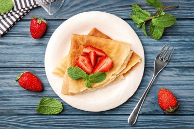 Plaka ince karabuğday krep ve ahşap masa üzerinde çilek ile