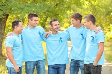 Young men in t-shirts with blue ribbons outdoors. Prostate cancer awareness concept clipart