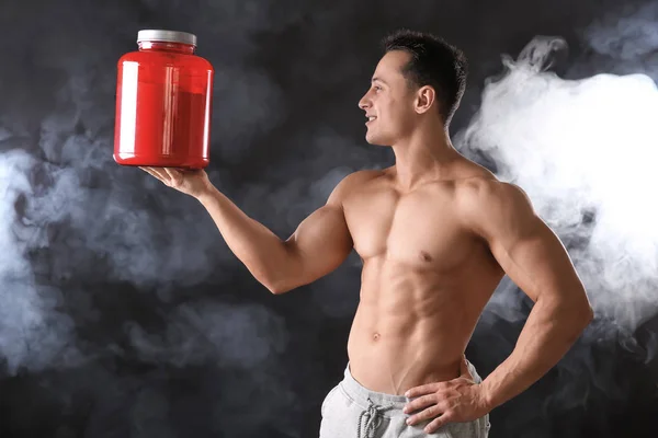 Sporty young man with jar of protein powder on black background — Stock Photo, Image