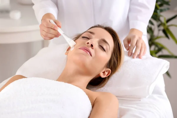 Beautician applying cream on young woman's face in spa salon — Stock Photo, Image