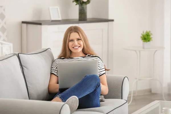 Evde koltukta istirahat ederken dizüstü bilgisayar kullanan güzel kadın — Stok fotoğraf