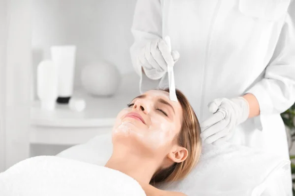 Kosmetikerin cremt Gesicht junger Frau im Wellness-Salon ein — Stockfoto