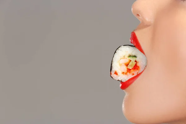 Mulher bonita com sushi rolar na boca em fundo cinza, close-up — Fotografia de Stock