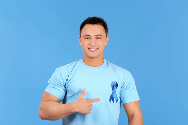 Молодий чоловік вказує на синю стрічку на футболку на кольоровому фоні. Концепція обізнаності про рак простати — стокове фото