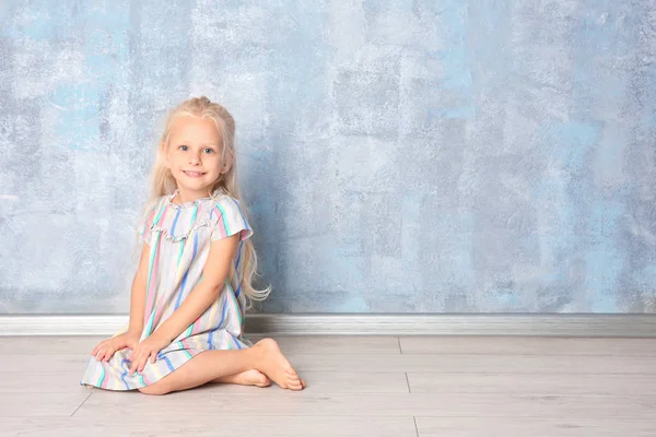 Menina bonito sentado perto de parede cinza — Fotografia de Stock