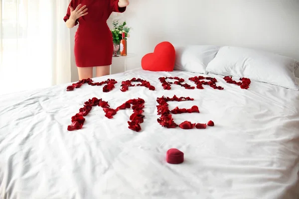 Idea para propuesta de matrimonio, mensaje MARRY ME hecha de pétalos de rosa en la cama y mujer emocionada en la habitación —  Fotos de Stock