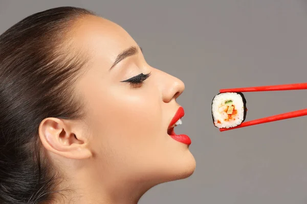 Mulher bonita com rolo de sushi em fundo cinza — Fotografia de Stock