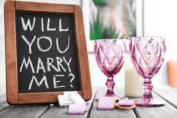Chalkboard with text WILL YOU MARRY ME and engagement ring on table — Stock Photo, Image