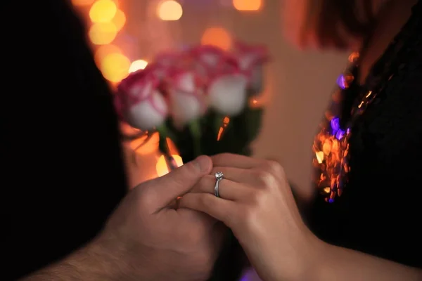 Homem segurando a mão de noiva com anel de noivado contra luzes embaçadas — Fotografia de Stock