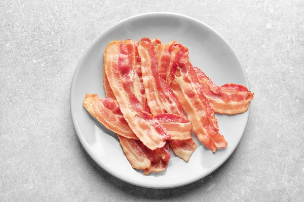 Tallrik med kokta bacon skivor på bord — Stockfoto