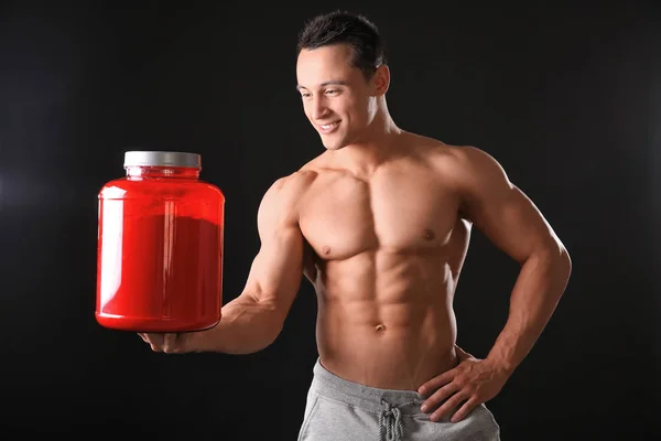 Jeune homme sportif avec pot de poudre de protéines sur fond noir — Photo